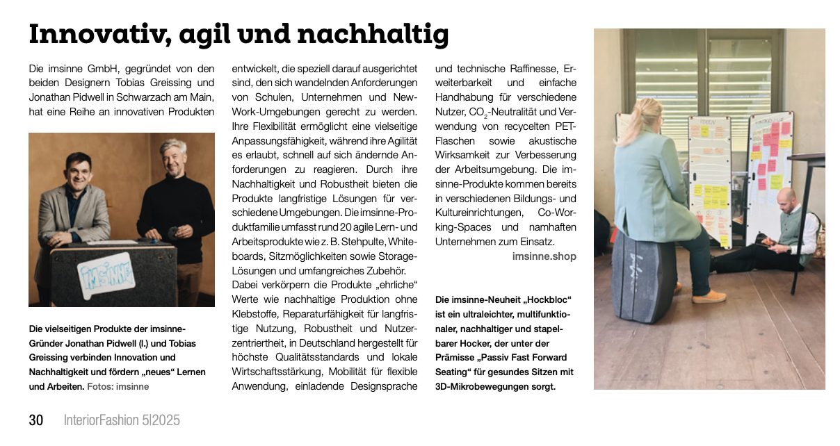 Eine moderne Büroszene in einem Artikel von InteriorFashion. Im Vordergrund sitzt eine Person auf einem grauen, runden imsinne "Hockbloc" und schaut auf ein Whiteboard. Im Hintergrund sind weitere Whiteboards mit Notizen und ein sitzender Mann zu sehen. Die Szene vermittelt ein agiles und flexibles Arbeitsumfeld.